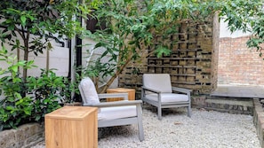 An outdoor seating area with two chairs and a wooden table, surrounded by gravel and greenery. - Be London - The Hampstead Residences (Greater London)