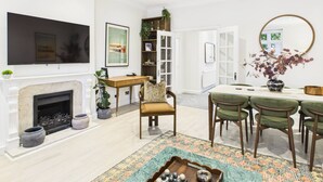 A modern living room with a fireplace, a flat-screen TV, a dining area with green chairs, and a large mirror. - Be London - The Hampstead Residences (Greater London)