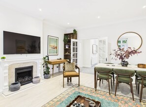 A modern living room with a fireplace, a flat-screen TV, a dining area with green chairs, and a large mirror. - Be London - The Hampstead Residences (Greater London)