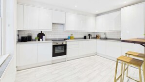 A modern kitchen with white cabinetry, a built-in oven, and a wooden bar stool. - Be London - The Hampstead Residences (Greater London)