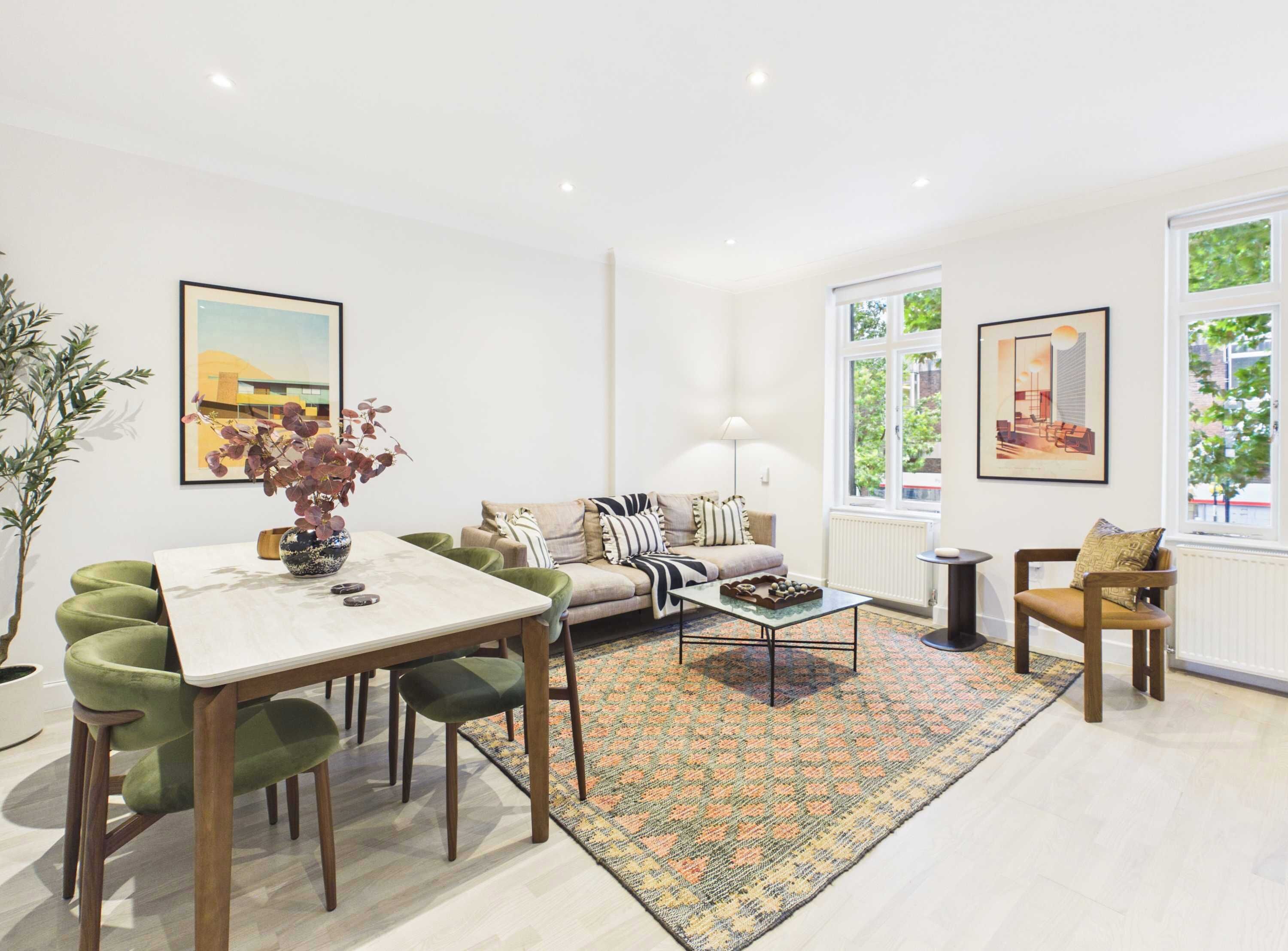 A modern living room with a dining table, sofa, and chairs, large windows, and artwork on the walls.