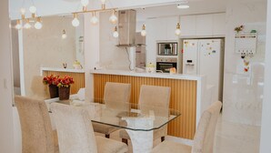A modern kitchen with a central island, white cabinetry, and a dining area with a glass table and chairs. - 3-Bedroom Spacious and Charming Apartment with Nature Views (Vila Velha)
