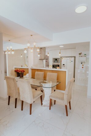 A modern kitchen with a central island, white cabinetry, and a dining area with a glass table and chairs. - 3-Bedroom Spacious and Charming Apartment with Nature Views (Vila Velha)