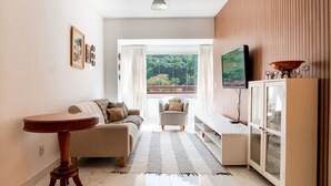 A living room with a sofa, a small table, a television, and a cabinet. - 3-Bedroom Spacious and Charming Apartment with Nature Views (Vila Velha)