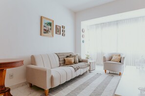 A living room with a sofa, armchair, and a table. - 3-Bedroom Spacious and Charming Apartment with Nature Views (Vila Velha)
