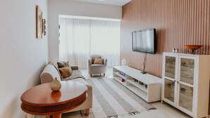 A modern living room with a sofa, a round table, a television, and a cabinet with glass doors. - 3-Bedroom Spacious and Charming Apartment with Nature Views (Vila Velha)