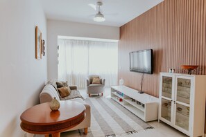 A modern living room with a sofa, a round table, a television, and a cabinet with glass doors. - 3-Bedroom Spacious and Charming Apartment with Nature Views (Vila Velha)