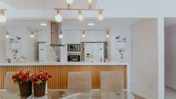 A modern kitchen with white cabinets, a central island, and a dining area with a glass table and chairs. - 3-Bedroom Spacious and Charming Apartment with Nature Views (Vila Velha)