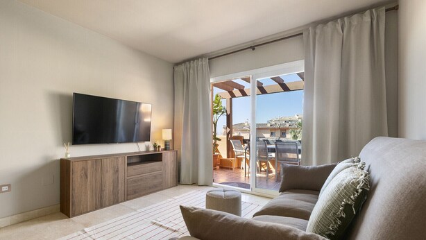 Ein Wohnzimmer mit Flachbildfernseher, Holzschrank, beiger Couch und Blick auf die Außenpatio.