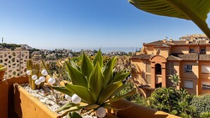 Ein Balkon mit einer Kakteenpflanze, weißen Papierlanternen und Blick auf Küstengebäude.