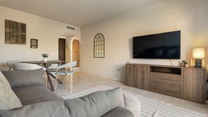 Ein Wohnzimmer mit Sofa, Fernseher, Holzschrank und einem Essbereich mit Stühlen und Tisch.