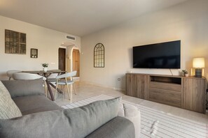 Ein Wohnzimmer mit Sofa, Fernseher, Holzschrank und einem Essbereich mit Stühlen und Tisch.