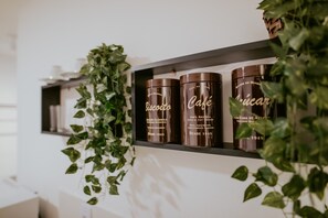 Ein Regal mit drei braunen Behältern, beschriftet mit 'Biscoito', 'Café' und 'Cachaca', und einer hängenden Pflanze.