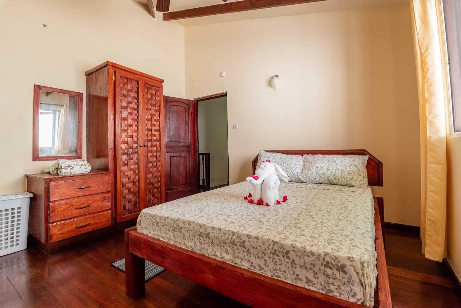 A bedroom with a wooden bed, a wardrobe, a mirror, and a small stuffed animal on the bed.