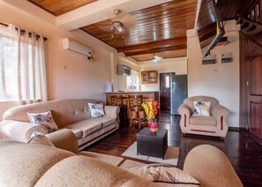 Una sala de estar con un sofá, sillones, una mesa de centro y una cocina al fondo.