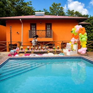 A swimming pool with a tiled deck, a building with a red roof, and a balloon arch.