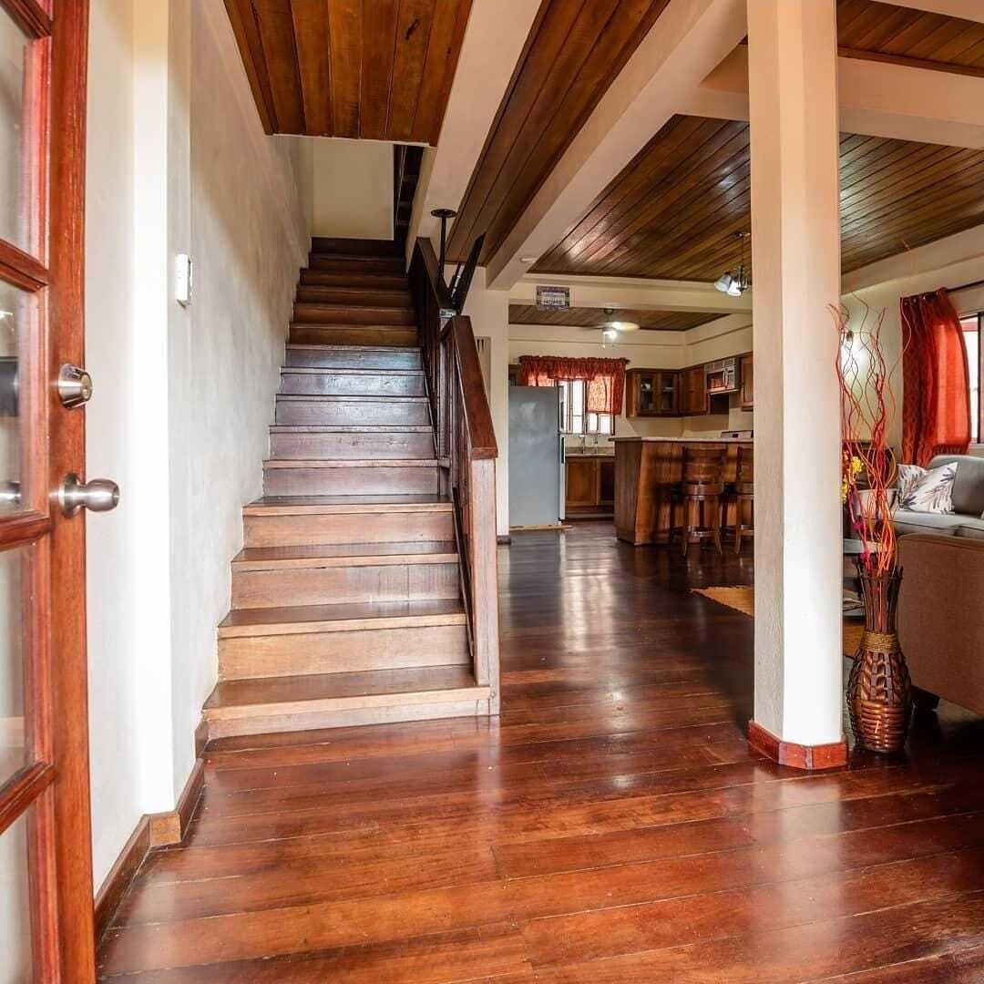 Una escalera de madera que lleva a una sala de estar con una cocina al fondo.