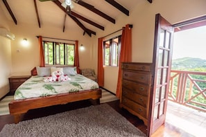 A bedroom with a bed, a dresser, and a balcony with a view.