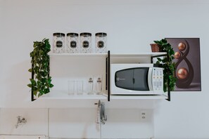 Eine Küche mit weißen Schränken, einer Mikrowelle und einem Regal mit Gläsern, beschriftet mit 'Açúcar', 'Café', 'Fielão' und 'Sal'.
