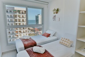 Ein Hotelzimmer mit zwei Betten, einem großen Fenster mit Blick auf Gebäude, einer Pflanze und einer Schmetterlingsdekoration.