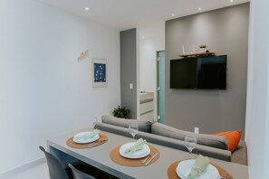 Ein moderner Essbereich mit einem Tisch für zwei Personen, einer grauen Couch und einem Wand-Fernseher.