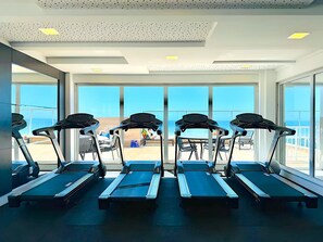 Ein Fitnessstudio mit Laufbändern und großen Fenstern mit Blick auf einen Strand.