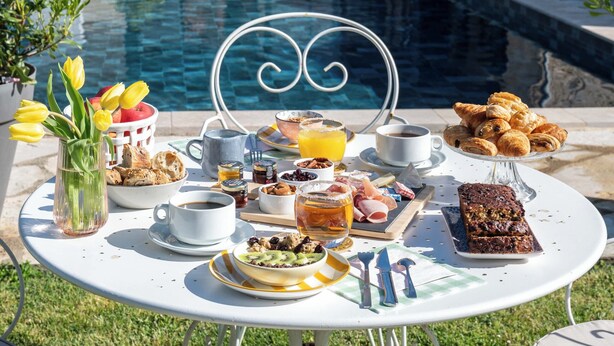 A poolside breakfast setup with a table, chairs, and a variety of food and drinks.