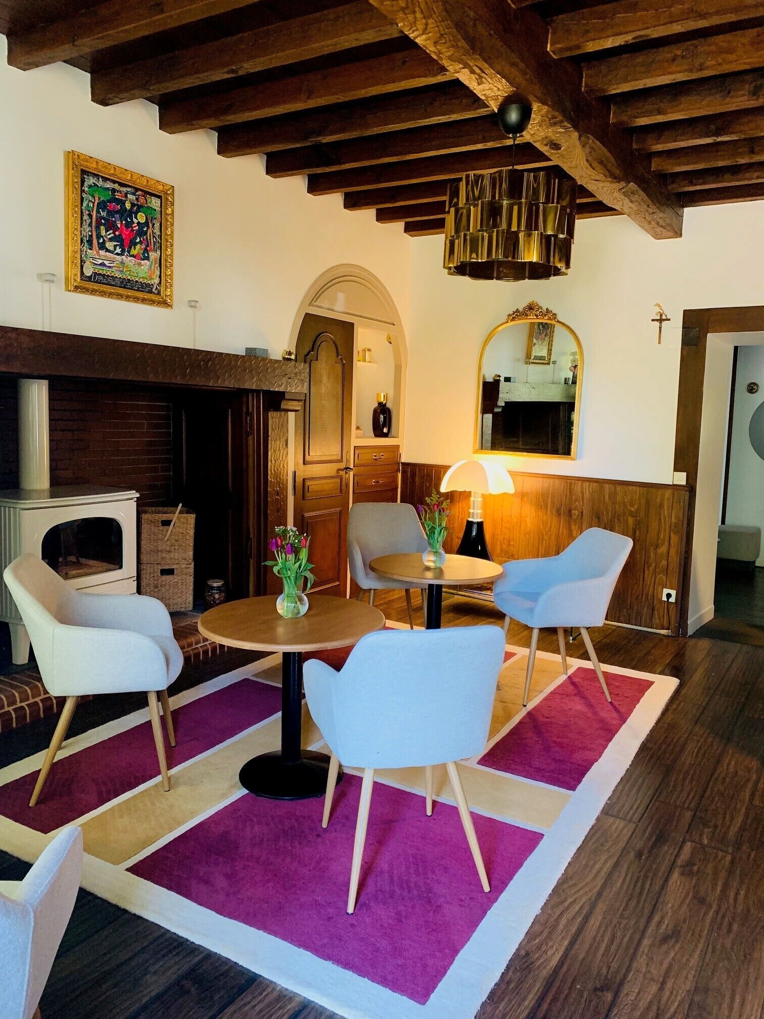 Una habitación con chimenea, vigas de madera en el techo, un espejo y una mesa con sillas.