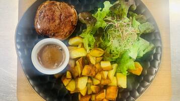 A plate with a grilled steak, roasted potatoes, a salad with greens and sprouts, and a small bowl of sauce.