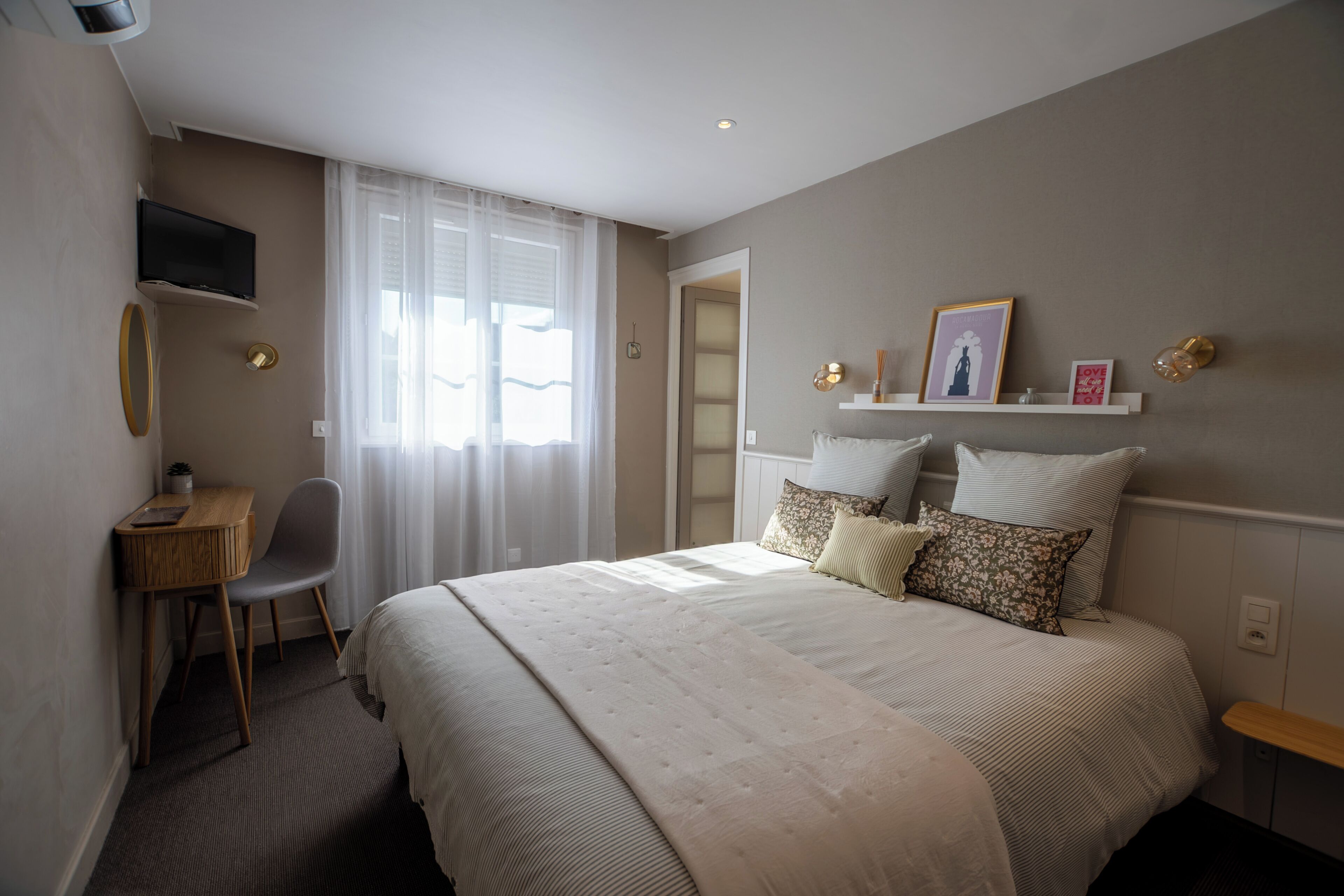 A bedroom with a bed, a desk, a chair, a TV, and a window with curtains.