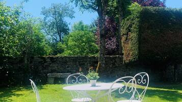 A white metal table and chairs set on a grassy lawn with a stone wall and trees in the background.
