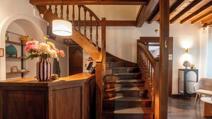 A wooden staircase with a railing, a wooden desk with a vase of flowers, and a chair in a room with wooden beams and a staircase.