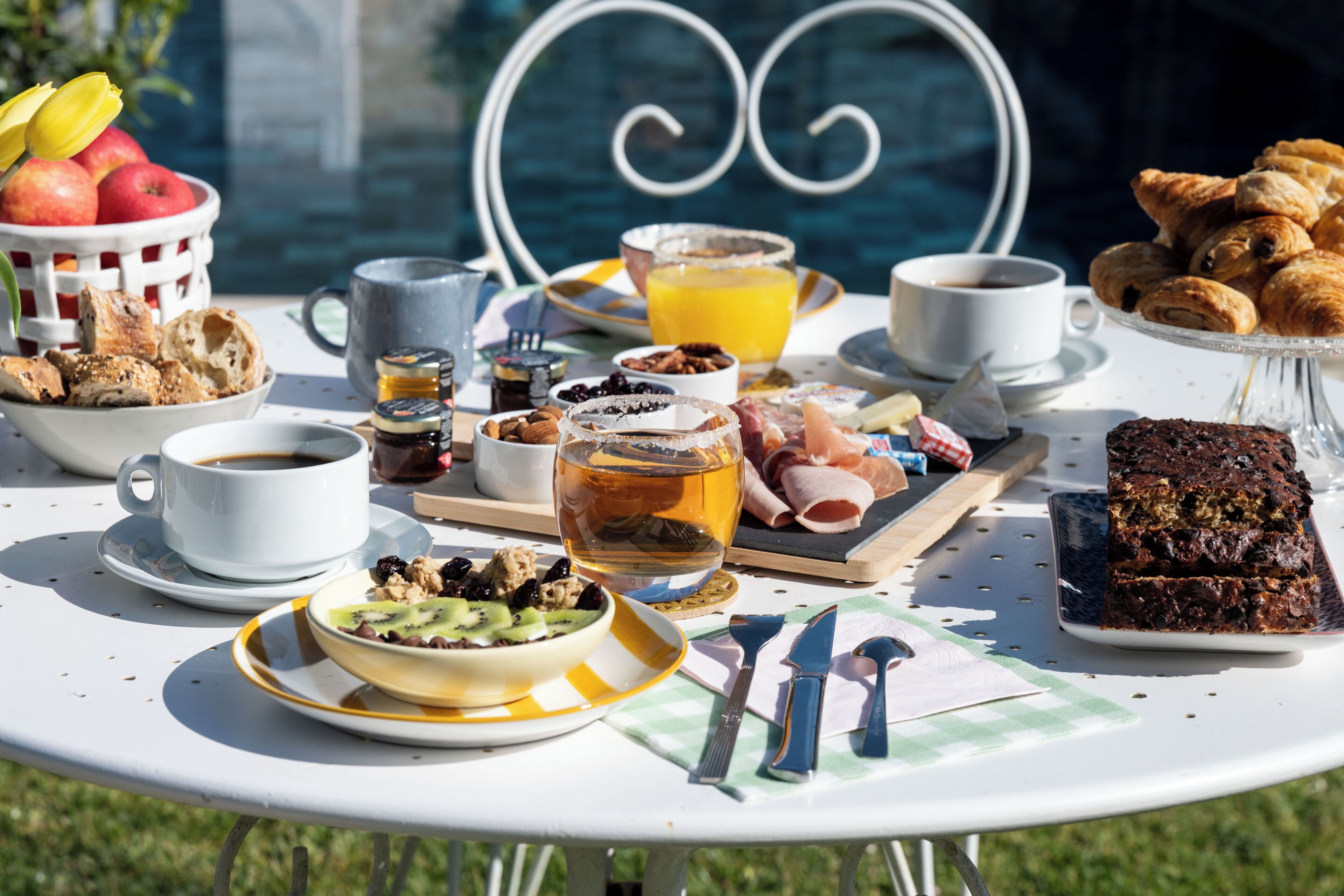 A breakfast table with various food items, a cup of coffee, and a bowl of fruit.