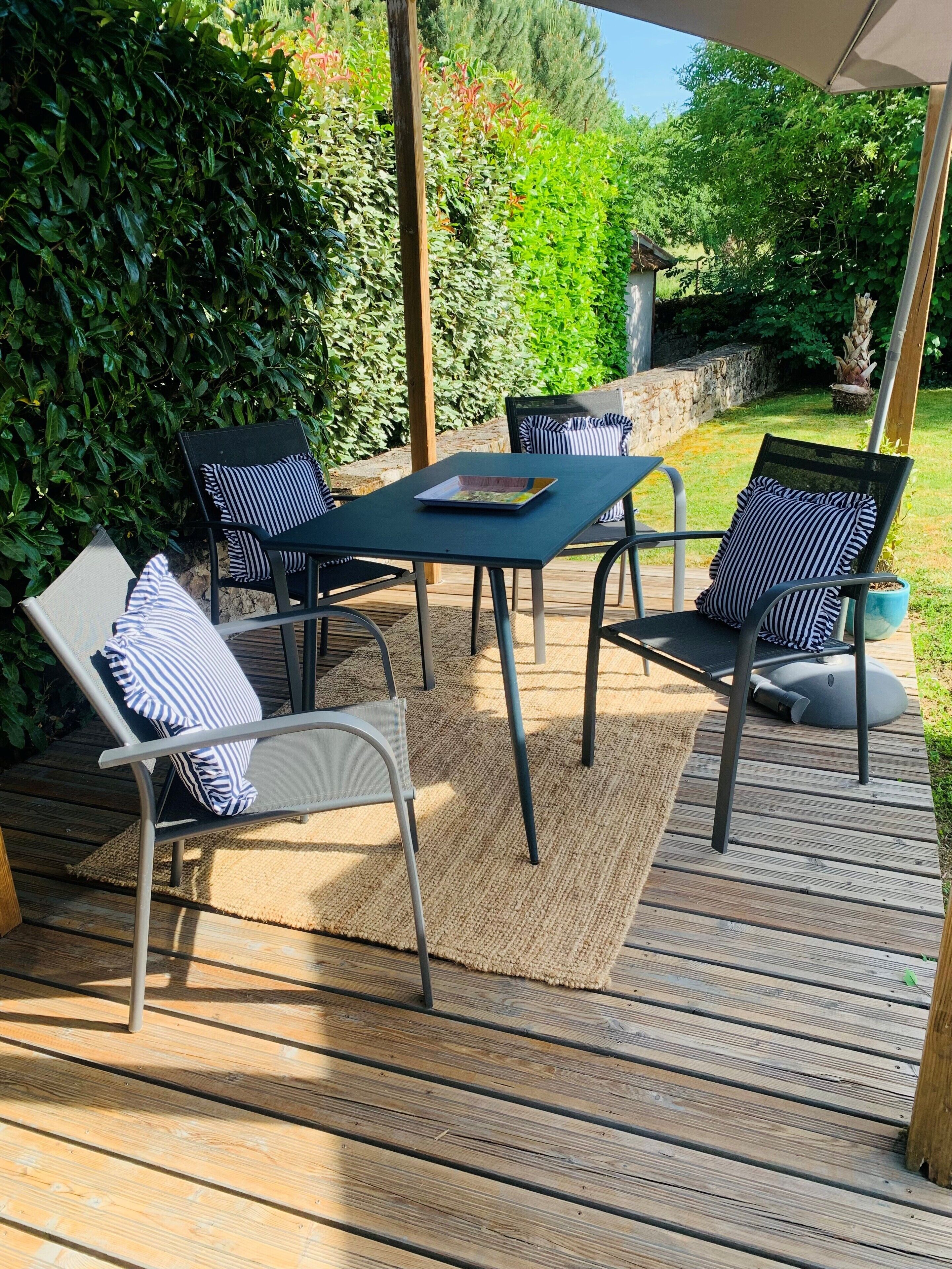 An outdoor patio with a table and chairs, surrounded by greenery.
