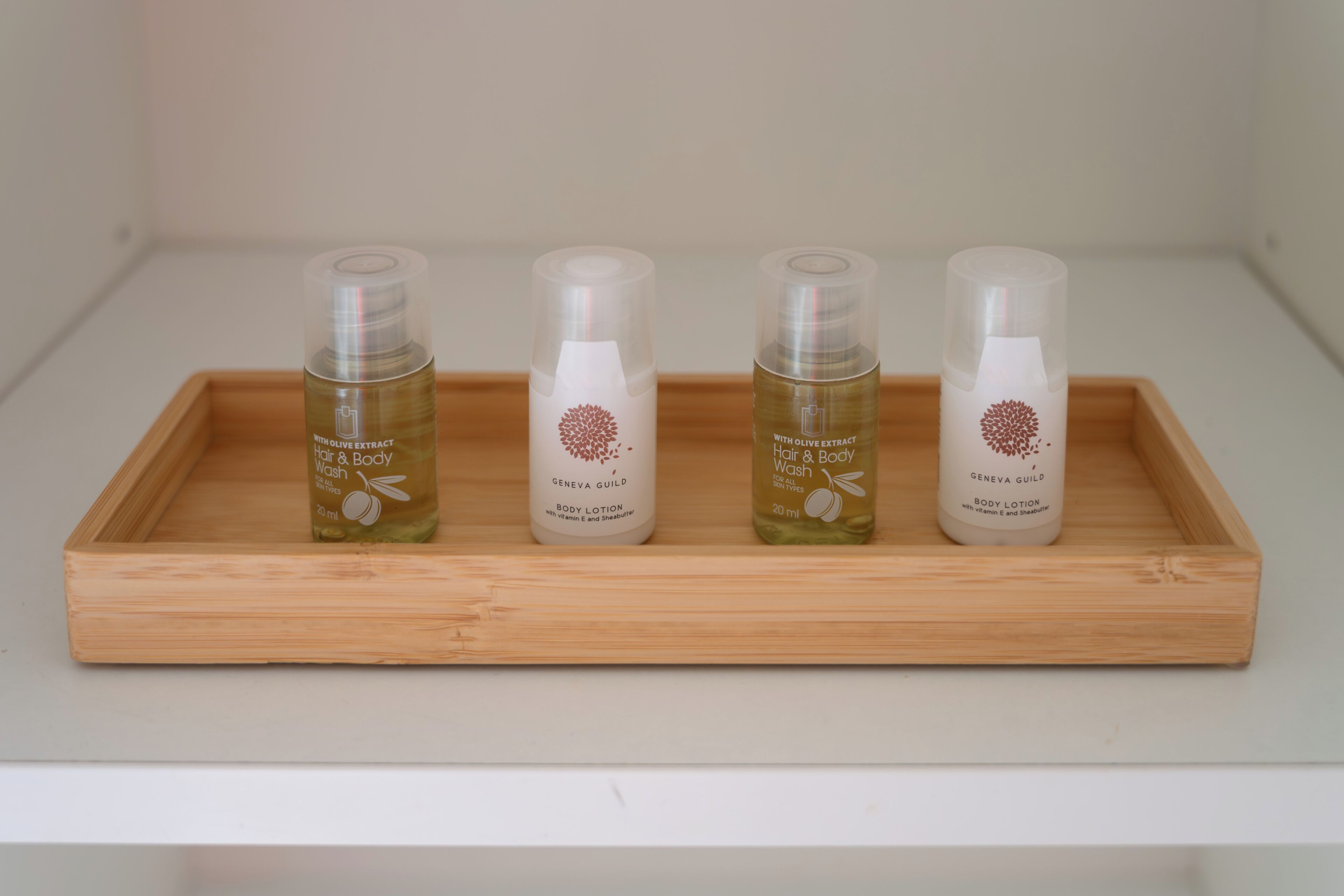 A wooden tray with four bottles of body lotion on a white shelf.