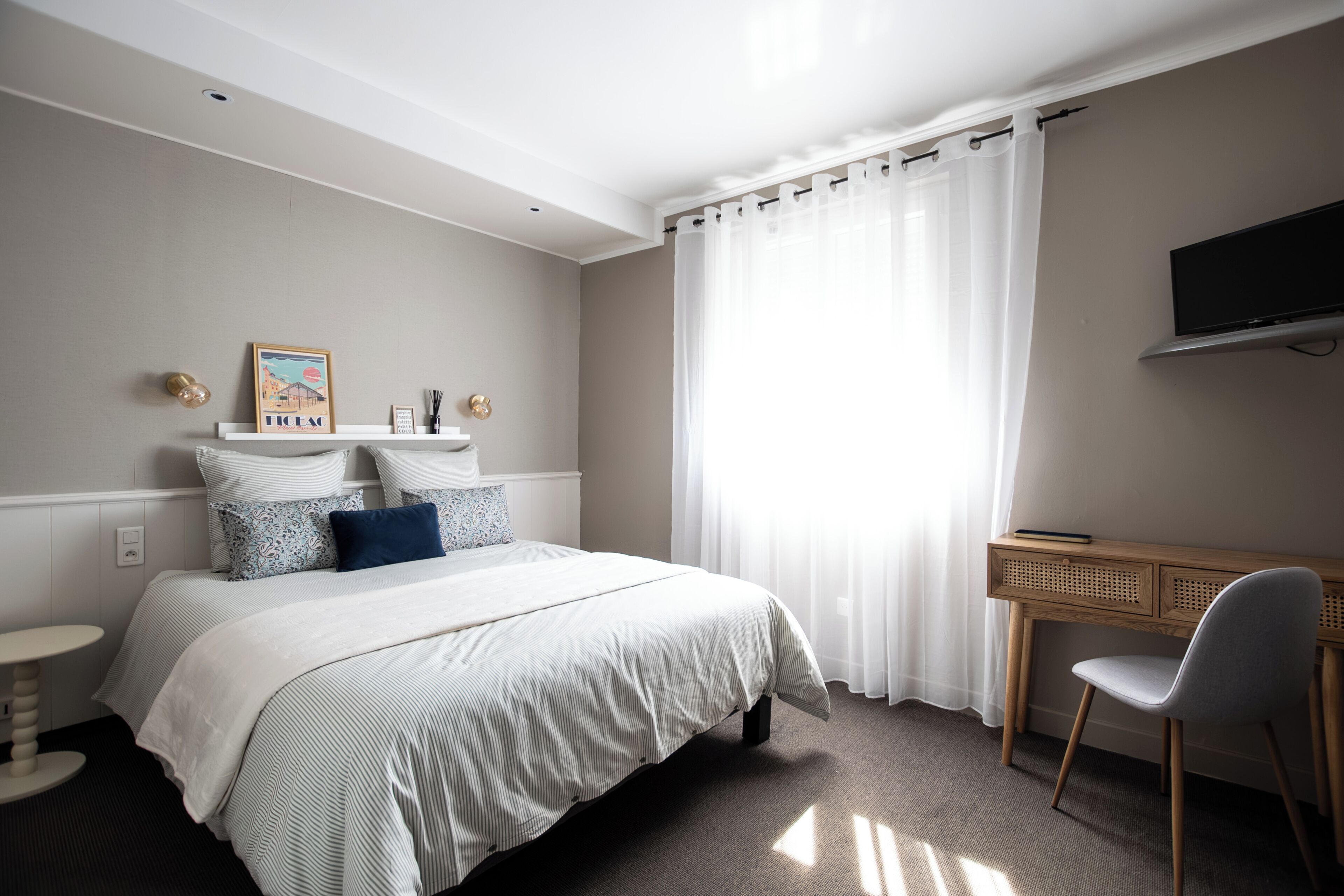 A bedroom with a bed, bedside tables, a desk, a chair, a television, and a window with curtains.