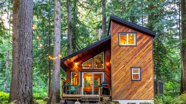 A cabin with a wooden exterior, large windows, and a porch area. - Barrel sauna, cedar cabin, woodstove (Deming)