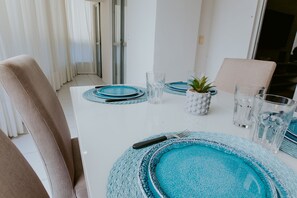 Ein Esstisch, gedeckt mit blauen Tischsets, klaren Gläsern und einem kleinen Topfpflanzen.