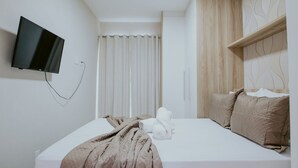 Una habitación de hotel con una cama, televisor montado en la pared, cortina y cabecera de madera.