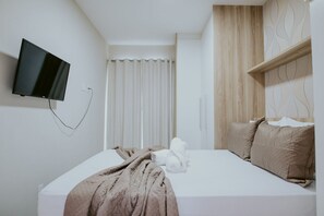 Ein Hotelzimmer mit Bett, Wandfernseher, Vorhang und Holz-Kopfteil.