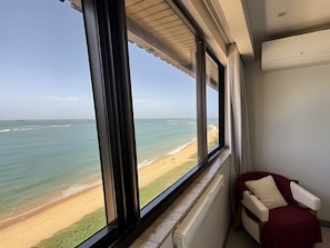 Ein Zimmer mit großem Fenster und Blick auf einen Strand, einem Heizkörper und einem Sessel mit Kissen.
