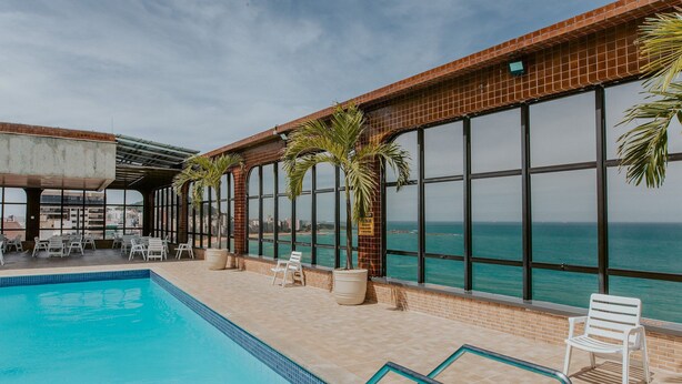 Ein Poolbereich mit Blick auf das Meer, Liegestühle und Topfpflanzen.