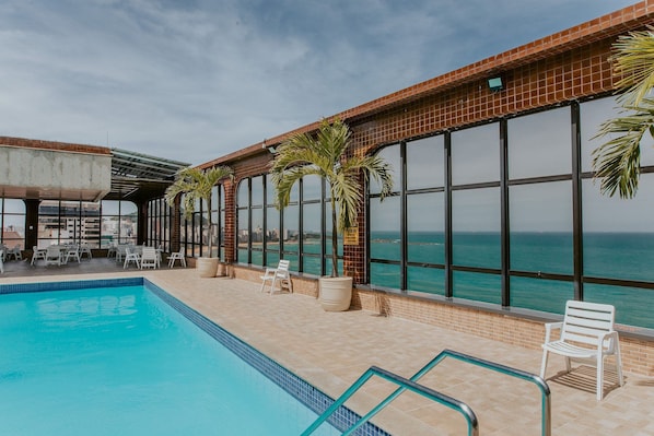 Ein Poolbereich mit Blick auf das Meer, Liegestühle und Topfpflanzen.