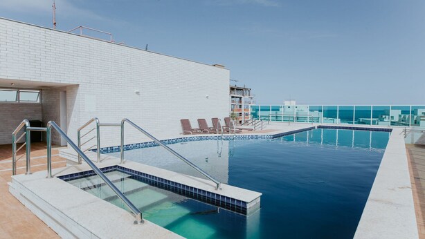 Ein Schwimmbecken mit Fliesen umrandet, ein weißes Gebäude und ein klarer Himmel.