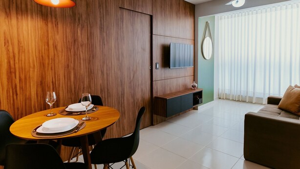 Ein modernes Wohnzimmer mit Essbereich, Holzvertäfelung, Deckenventilator, Flachbildfernseher und einem großen Fenster mit Jalousien.