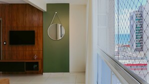 Ein Zimmer mit Fernseher, einem runden Spiegel, einem Holzschrank und Blick durch ein Fenster.
