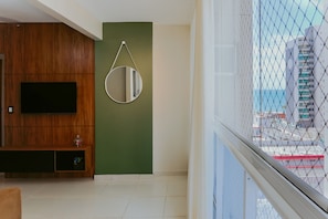 Ein Zimmer mit Fernseher, einem runden Spiegel, einem Holzschrank und Blick durch ein Fenster.