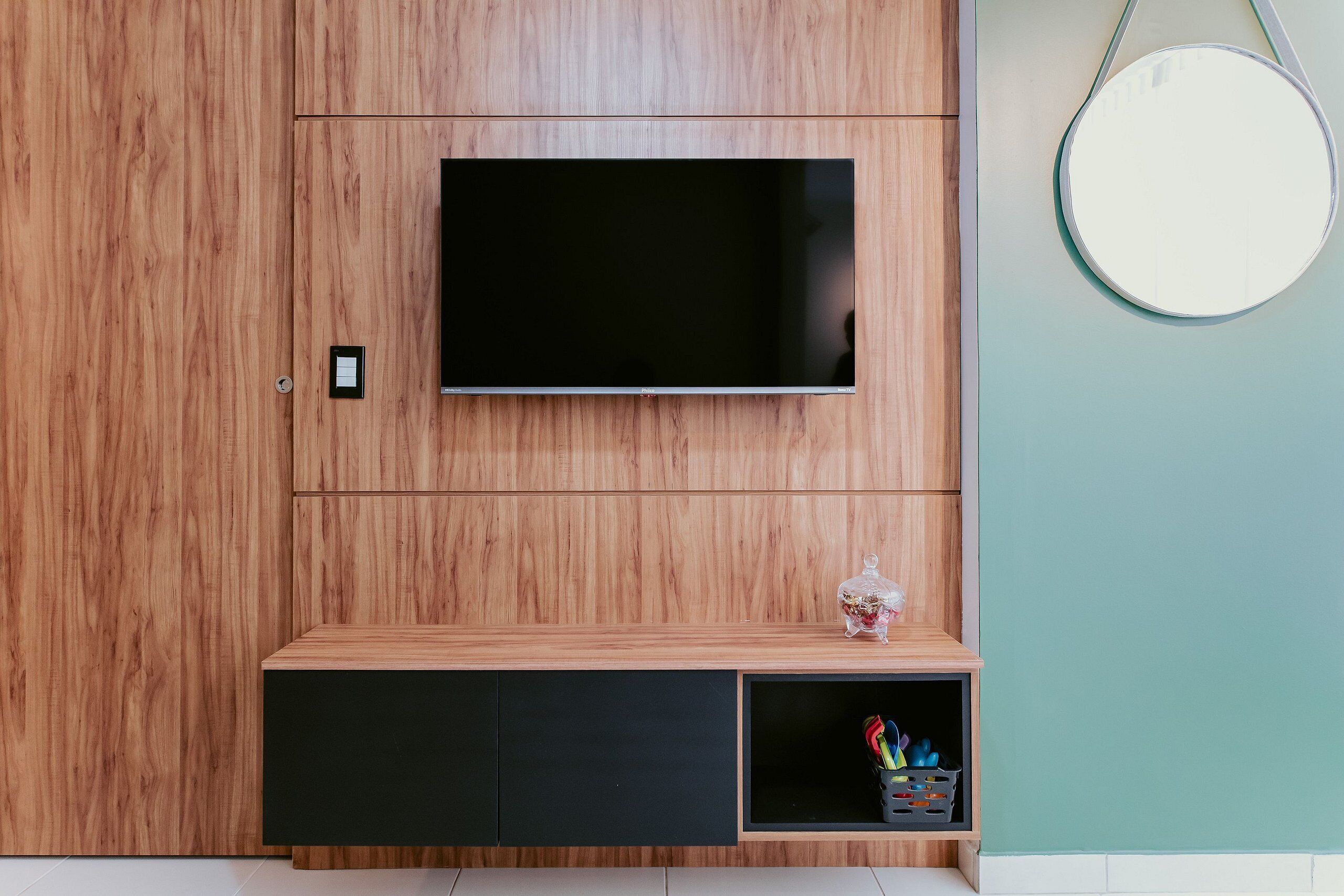 Eine Holzwand mit einem flachbildfernseher, der über einer schwarzen Unterhaltungsecke angebracht ist.