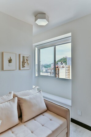 A modern living room with a sofa, a window with a city view, and two framed artworks on the wall. - Cozy Steps from the Sea | Costa Beach (Vila Velha)