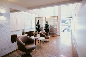 A modern lobby with leather armchairs, a small table with a plant, and a Christmas tree. - Cozy Steps from the Sea | Costa Beach (Vila Velha)